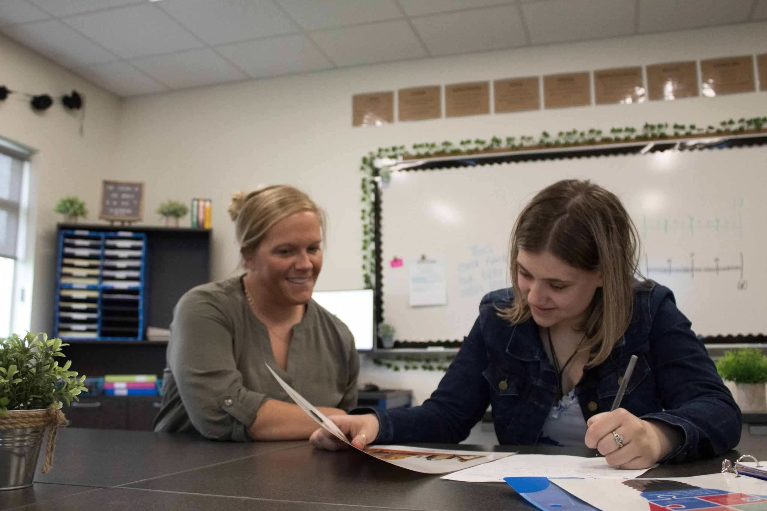 Teacher guiding a student with personalized support during a classroom activity, fostering independence at OPTIONS Transitions to Independence.